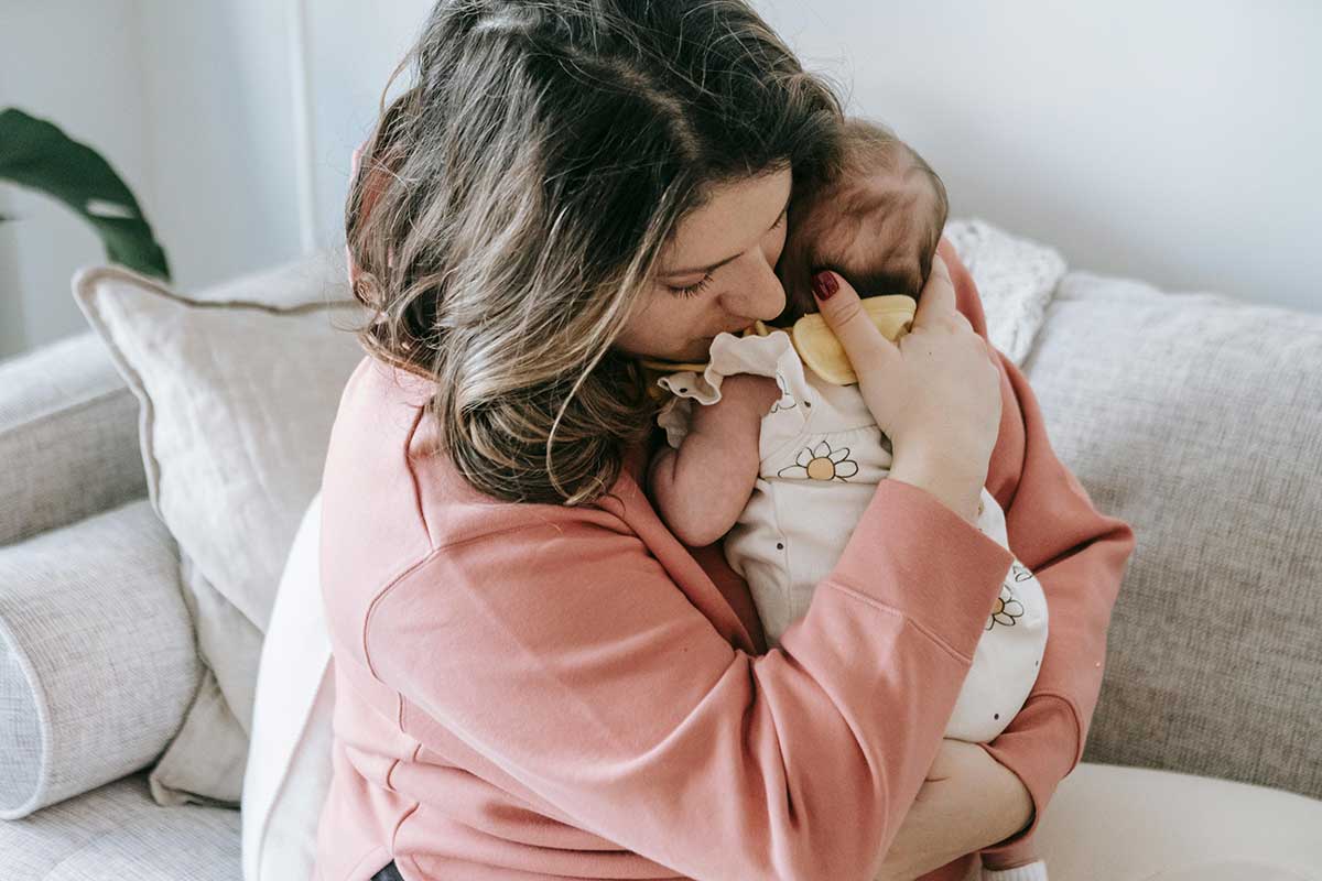 Mother Embracing Baby Tenderly In Bedroom