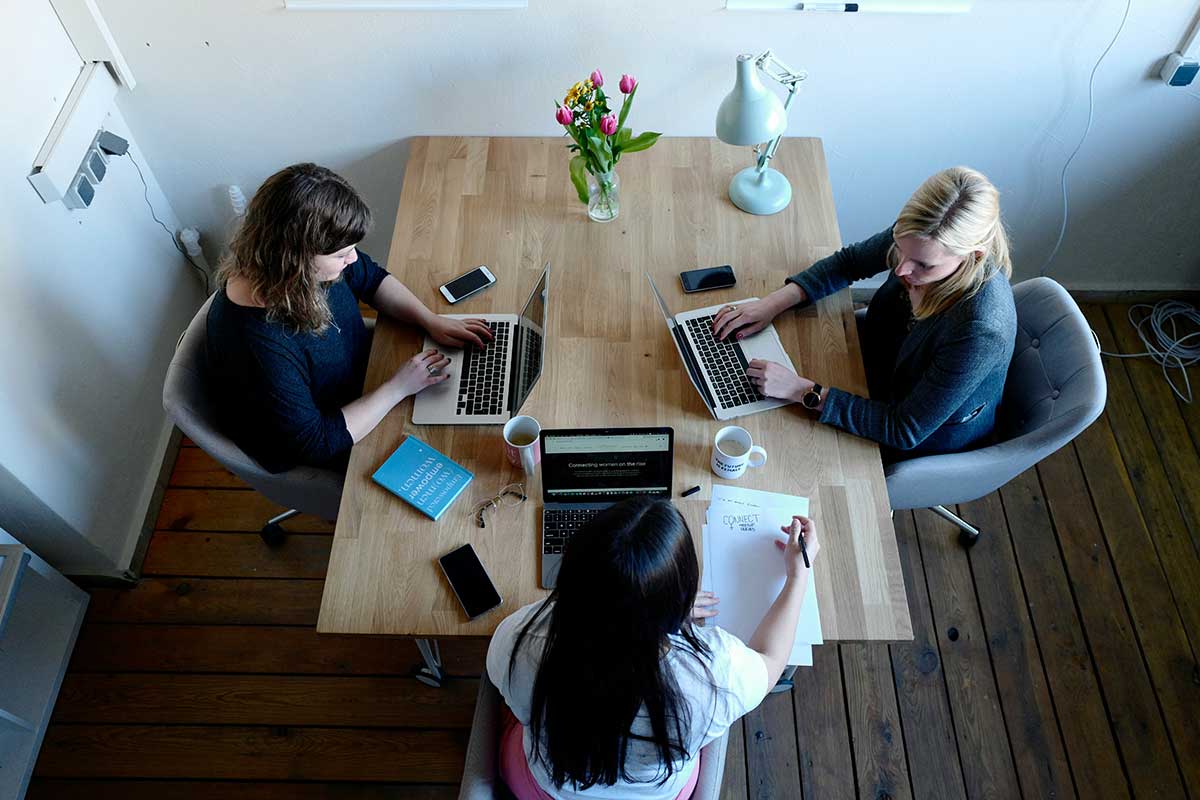 Three Women Sitting Around A Table With Laptops